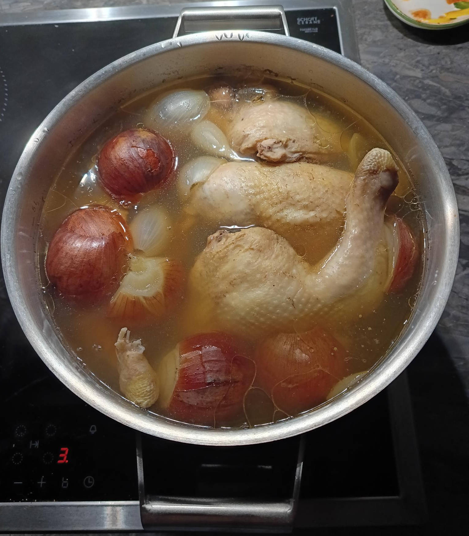 Chicken legs, garlic, and onions simmer in a large stainless steel pot with boiling water.